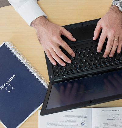 Vista superior de las manos de un hombre tecleando en un computador, con un libro de Grupo Argos sobre la mesa